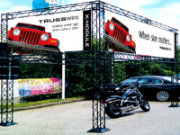 Stendo konstrukcija lauke, reklaminiai baneriai viršuje, motociklas apačioje