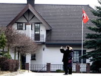 Красный флаг с бантом, поднятый на белом флагштоке рядом со зданием.