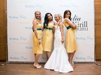 Keturios moterys pozuoja vestuvinei fotosesijai prie foto stendo sienos