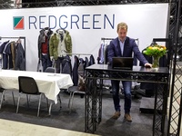 A clothing exhibition, a man at a table, a stand at the back, a graphic poster with a company logo